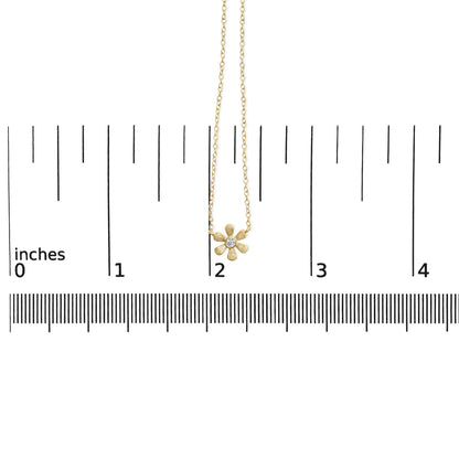 Yellow metal necklace with a flower-shaped pendant featuring a round white gemstone in the center, shown hanging on a ruler for size reference, front view.