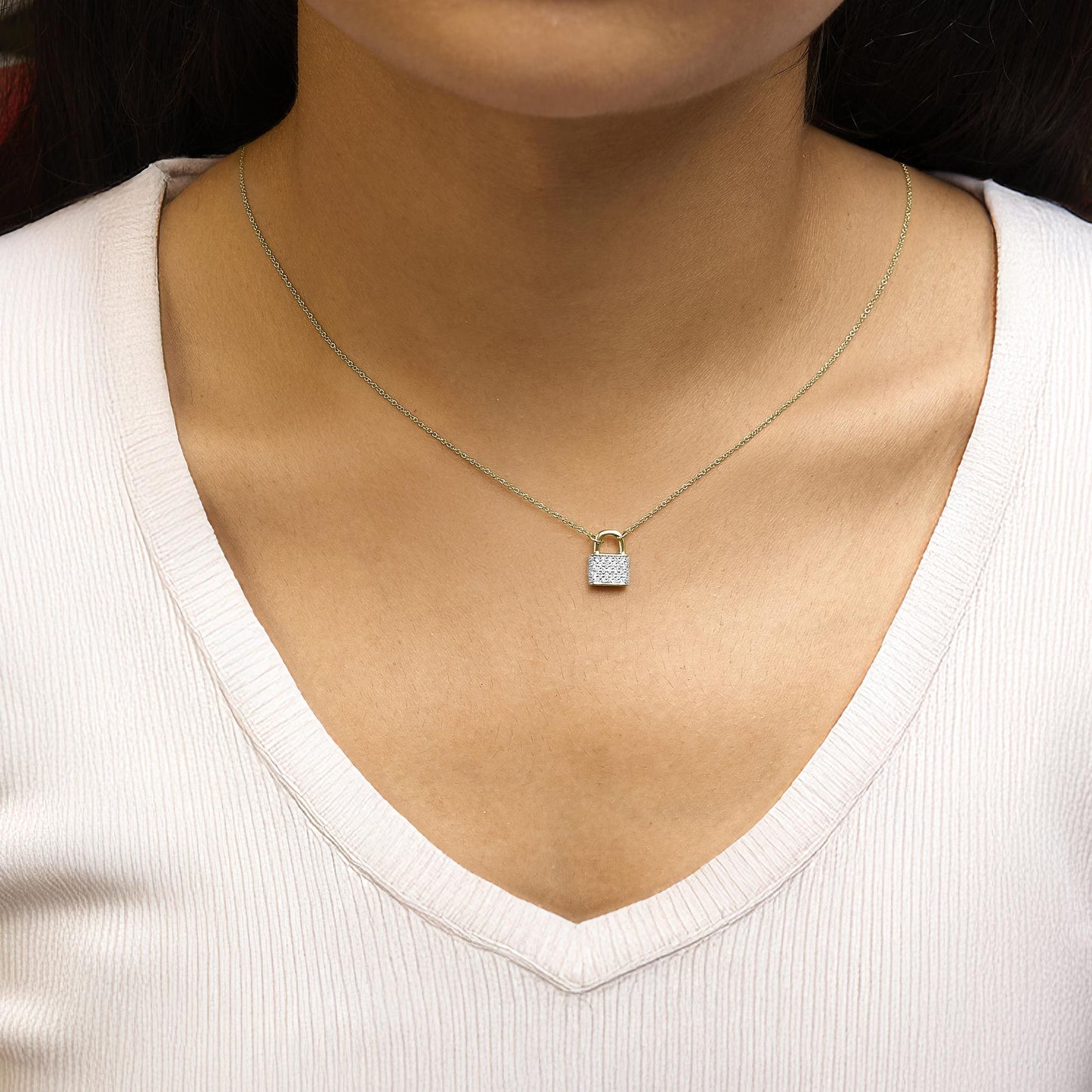 Close-up front view of a yellow metal necklace with a padlock-shaped pendant featuring round white gemstones, worn on a model.