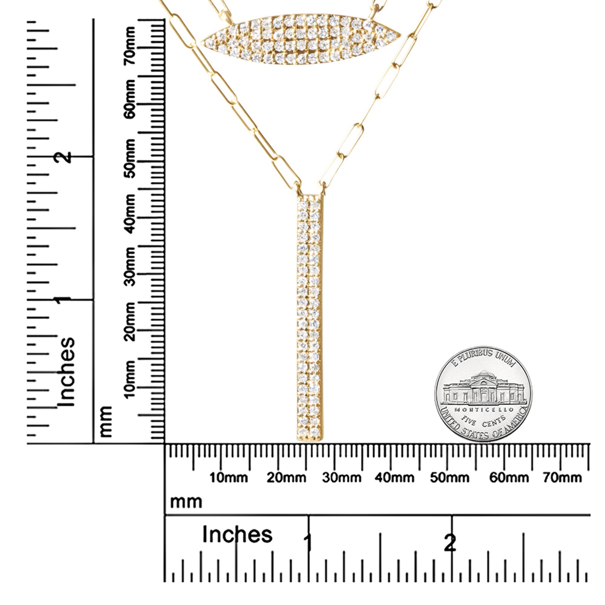 Close-up front view of a yellow metal necklace with two pendants featuring multiple round white gemstones in prong settings, displayed on a ruler and next to a coin for size reference.