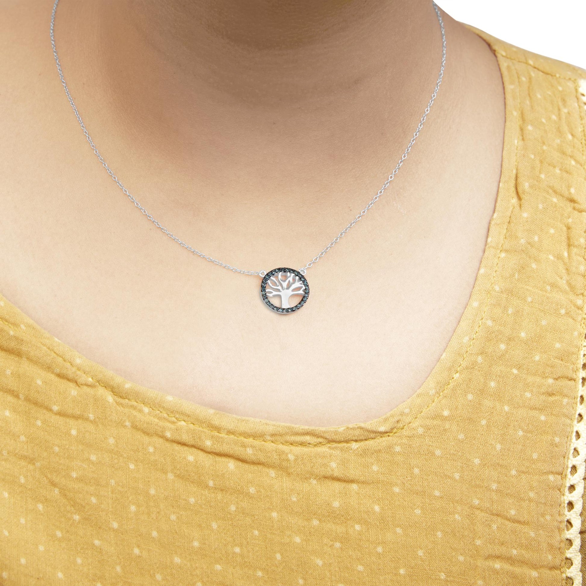 Close-up front view of a white metal necklace on a model, featuring a round pendant with a tree design surrounded by prong-set blue gemstones.