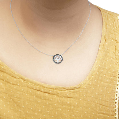 Close-up front view of a white metal necklace on a model, featuring a round pendant with a tree design surrounded by prong-set blue gemstones.