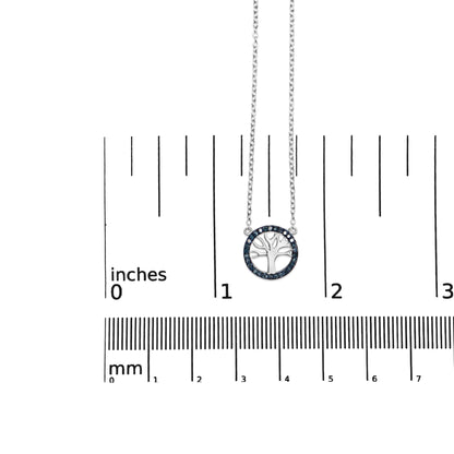 White metal necklace with round prong-set blue gemstones forming a circle around a tree-shaped pendant, shown from a top-down angle on a ruler for size reference.