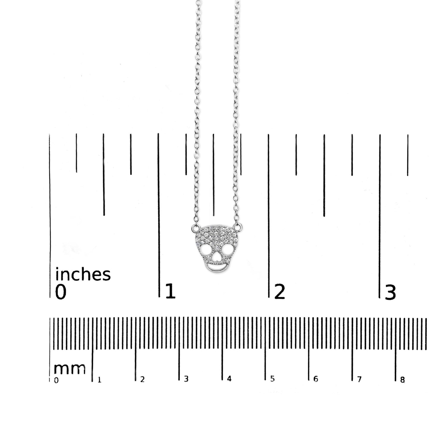 White metal necklace with a skull-shaped pendant adorned with small round white gemstones in prong settings, shown on a ruler for size reference, front view.