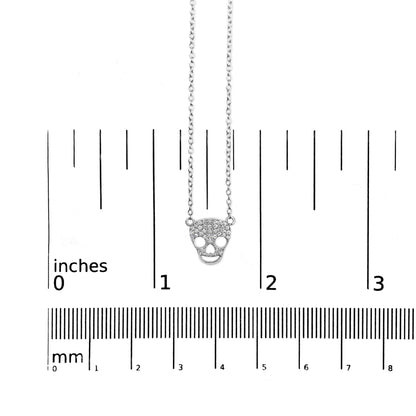 White metal necklace with a skull-shaped pendant adorned with small round white gemstones in prong settings, shown on a ruler for size reference, front view.