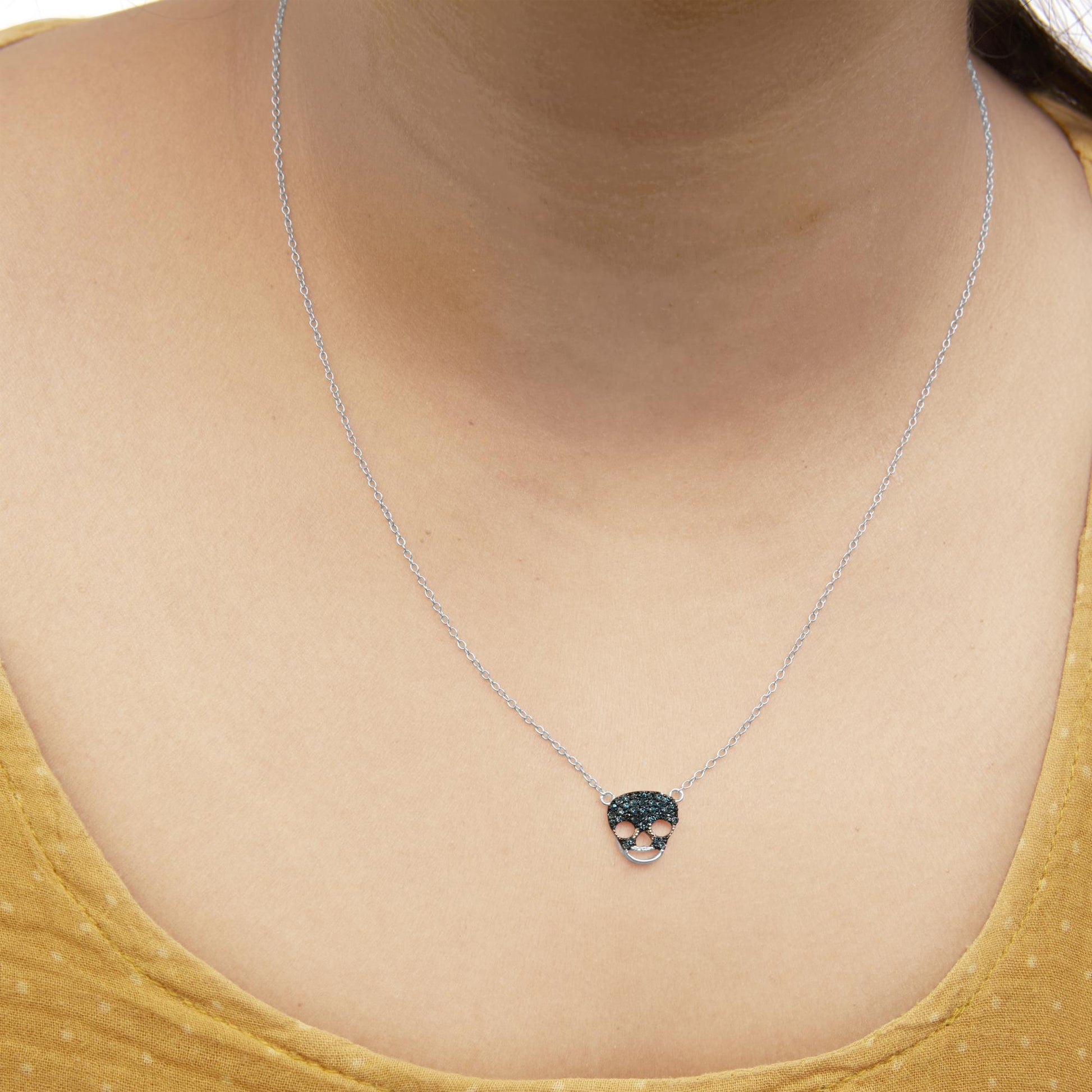 Close-up front view of a white metal necklace with a skull-shaped pendant set with blue round gemstones, worn on a model.