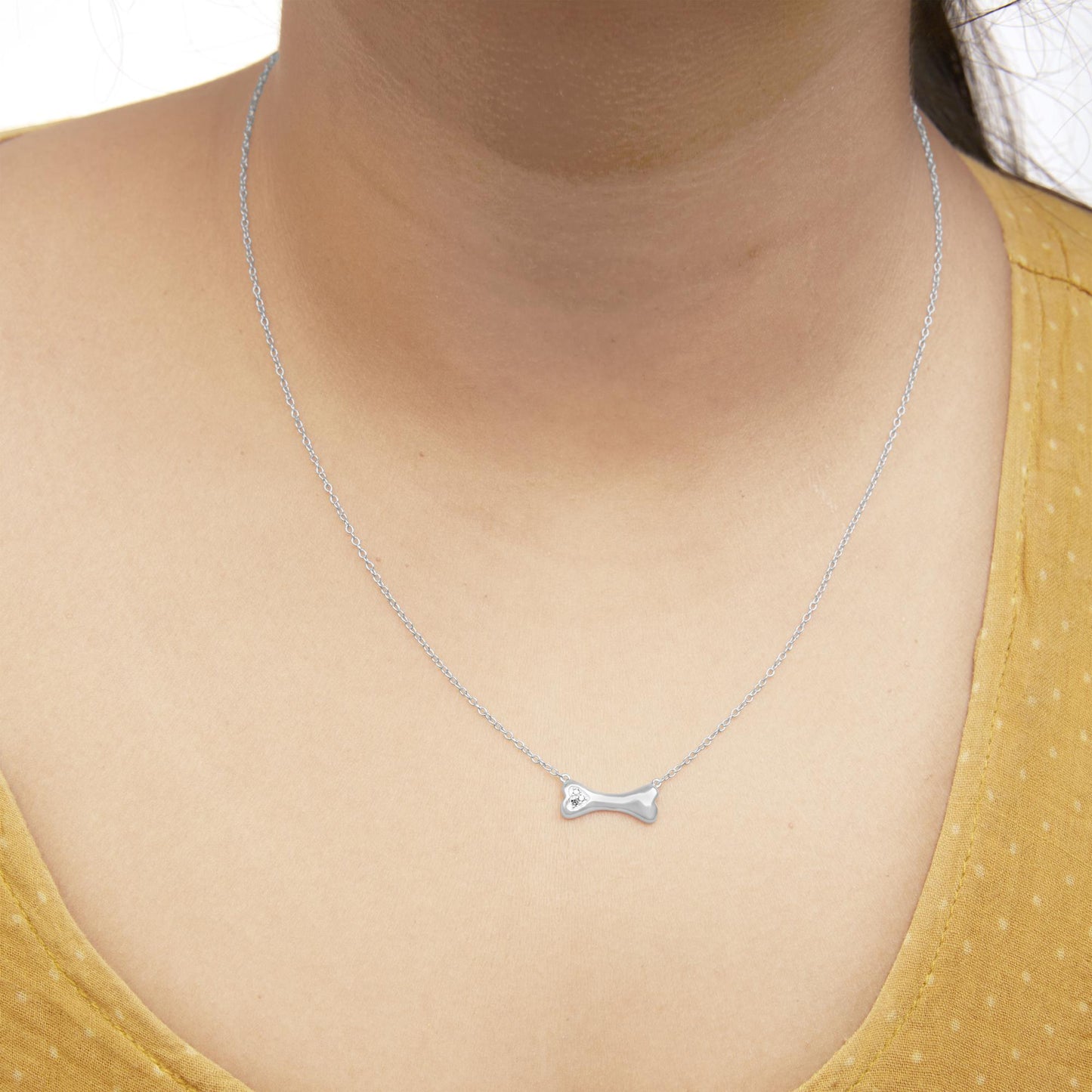 Close-up front view of a white metal necklace with a bone-shaped pendant featuring three round white gemstones in prong settings, worn on a model.