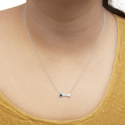 Close-up front view of a white metal necklace with a bone-shaped pendant featuring three round blue gemstones in prong setting, worn on a model.