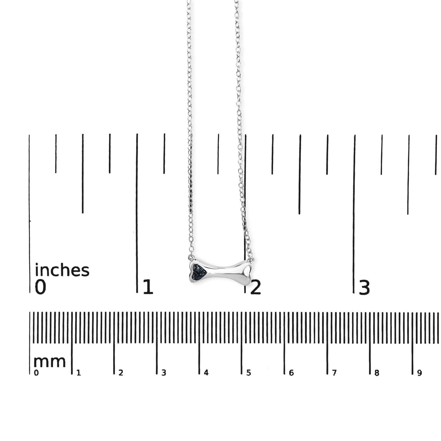 Front view of a white metal bone-shaped necklace with three blue round gemstones set in prongs, shown on a ruler for size reference.
