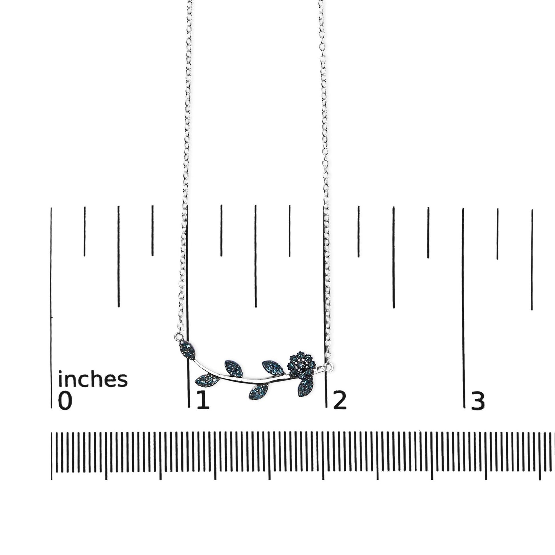 White metal necklace with a floral and leaf design set with blue round gemstones, shown flat on a ruler for size reference, front-facing angle.