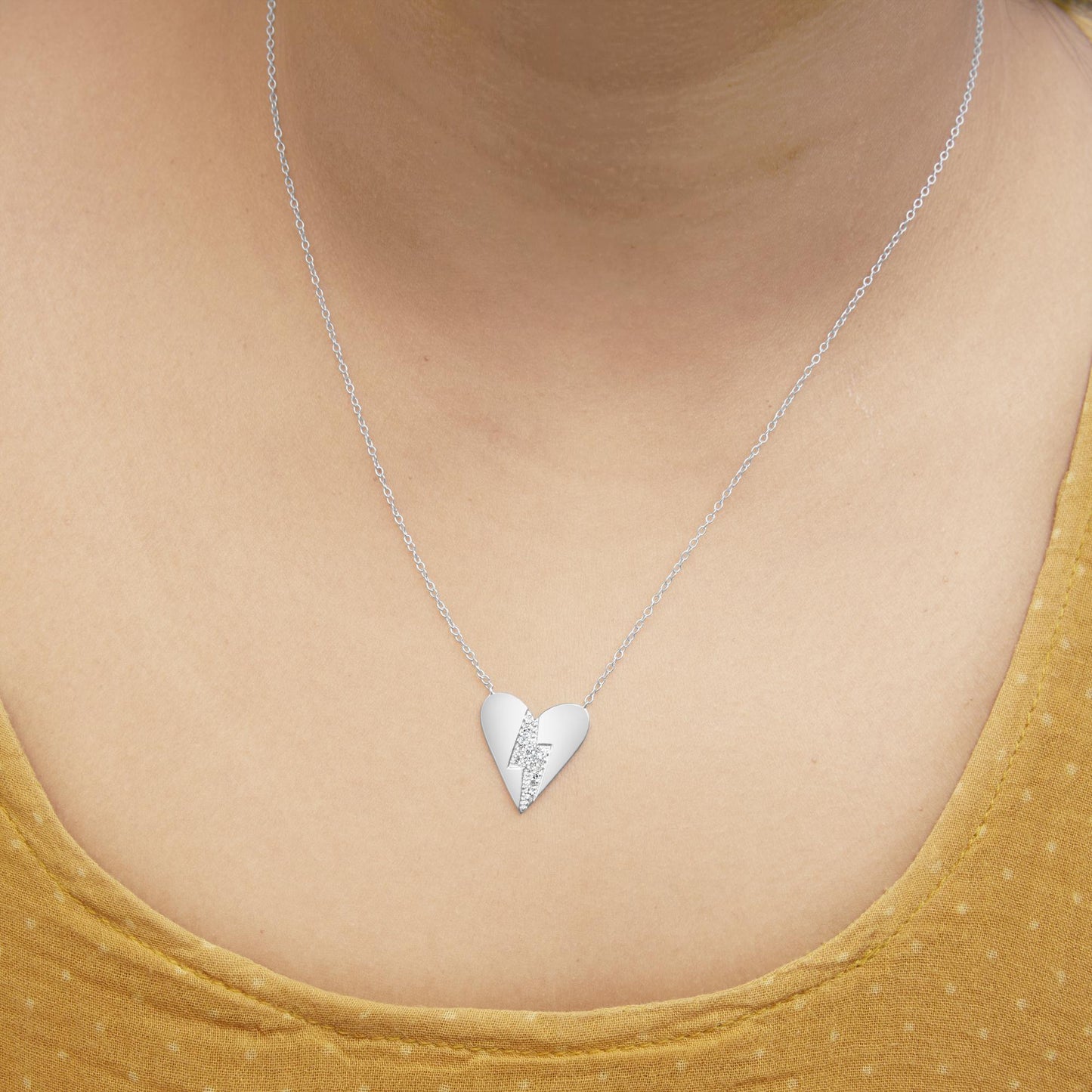 White metal necklace with a heart-shaped pendant featuring a lightning bolt accent set with round white gemstones, shown on a model from the front.
