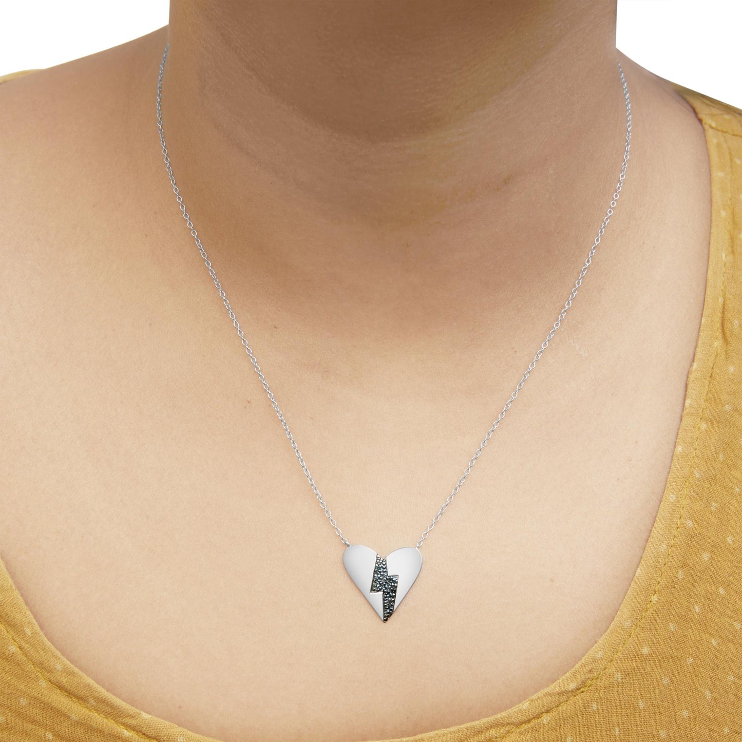 White metal heart-shaped necklace with a lightning bolt design set with round blue gemstones, worn on a model, front view.