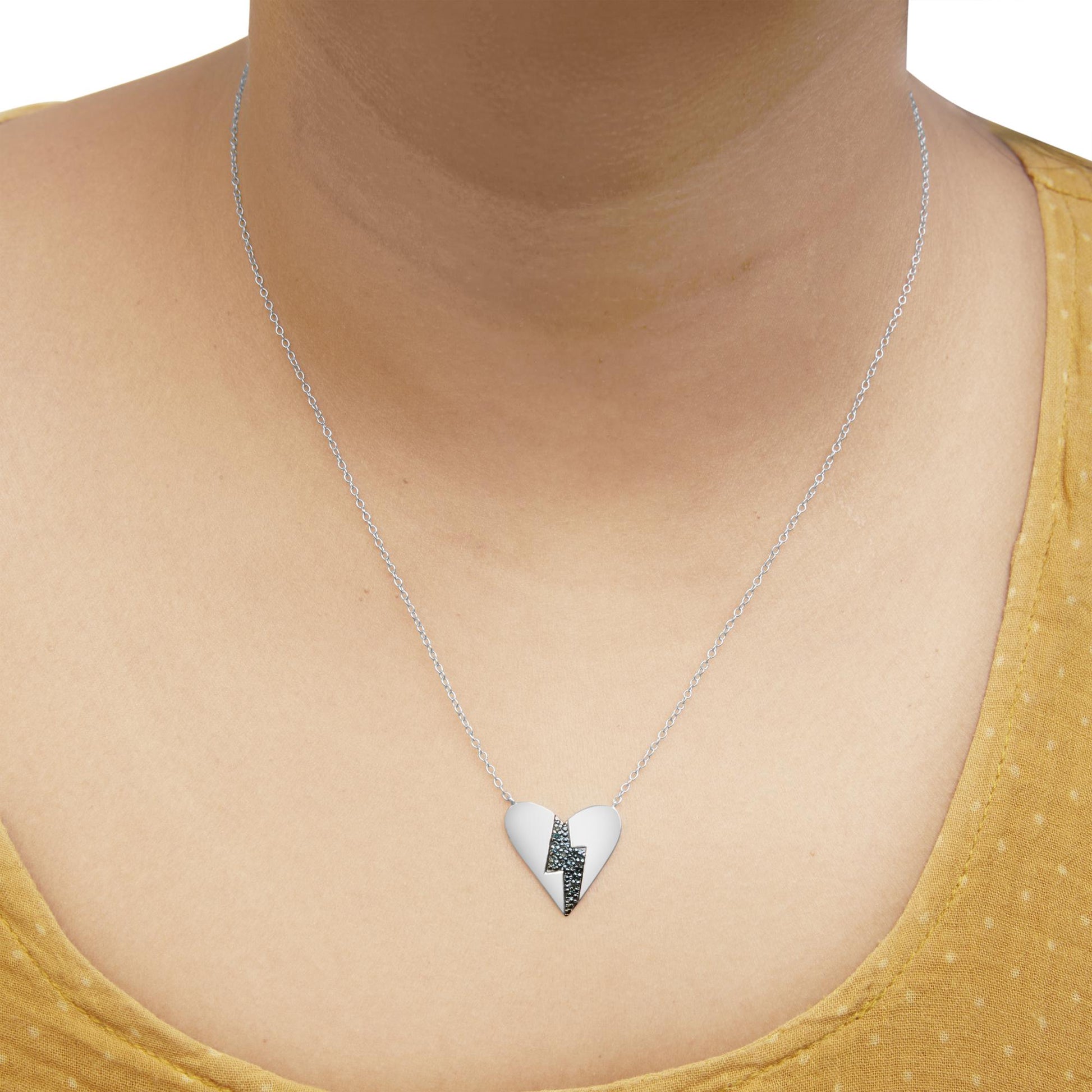 White metal heart-shaped necklace with a lightning bolt design set with round blue gemstones, worn on a model, front view.