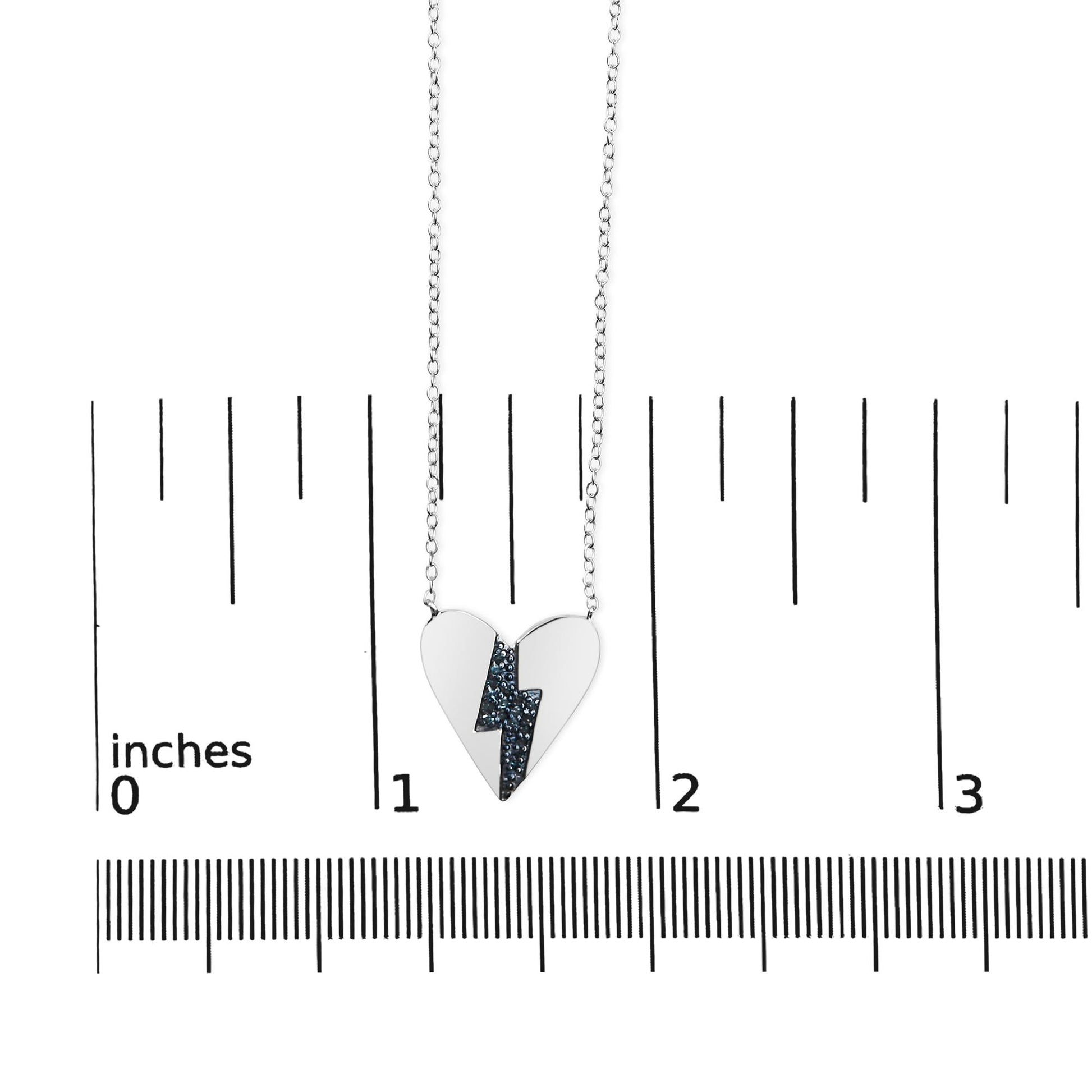 White metal heart-shaped necklace with a blue gemstone lightning bolt design, hanging on a chain, shown from the front on a ruler for size reference.
