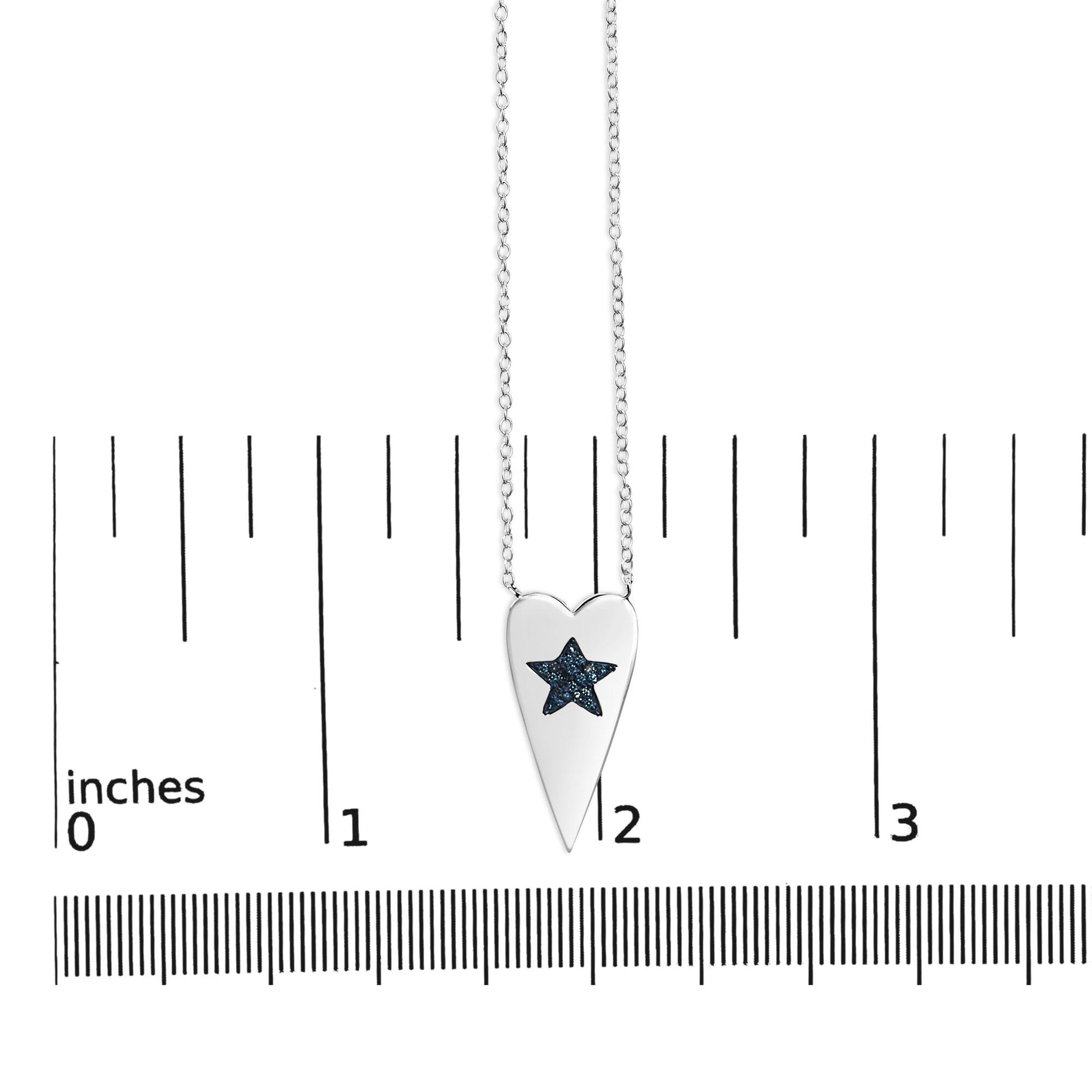 White necklace with a pointed heart-shaped pendant featuring a star-shaped cluster of blue round gemstones, shown hanging centered on a ruler scale from a front angle.
