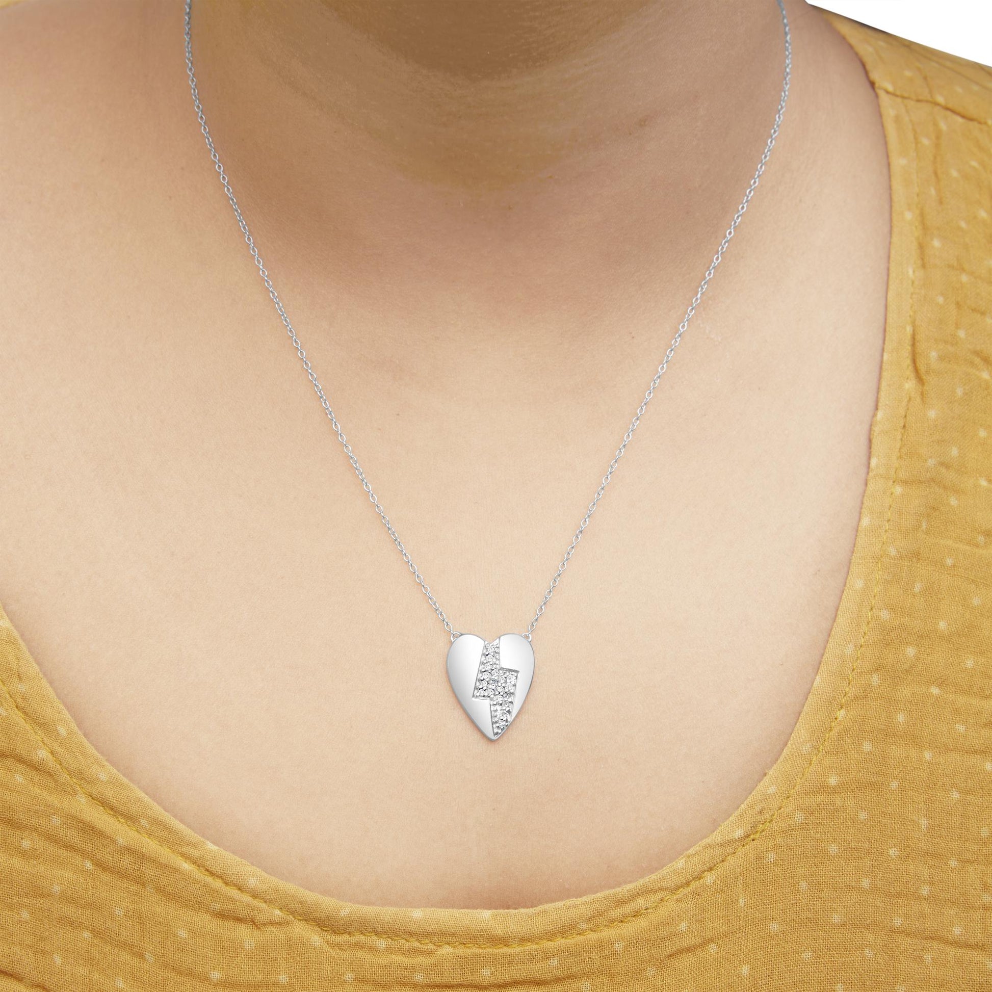 White metal heart-shaped necklace with a lightning bolt design featuring round white gemstones in a prong setting, worn on a model, front view.