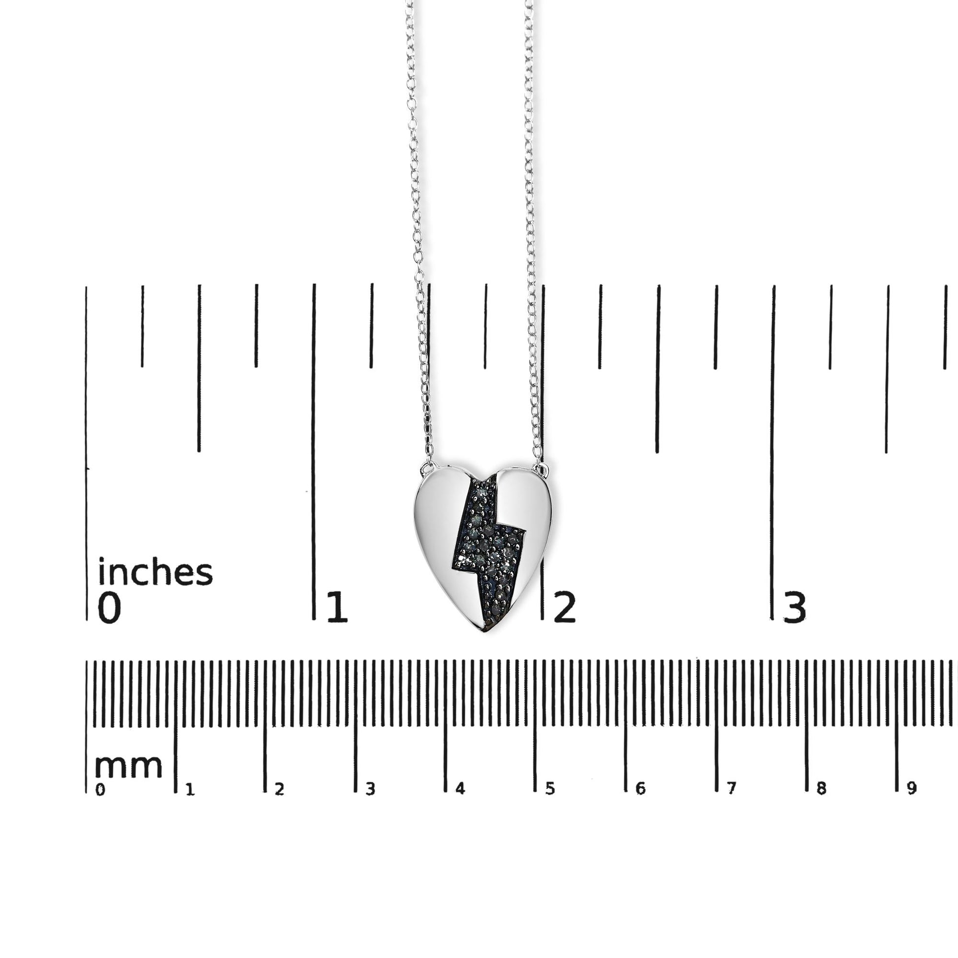 White metal heart-shaped necklace pendant with a zigzag design filled with blue round prong-set gemstones, shown from the front on a ruler for size reference.