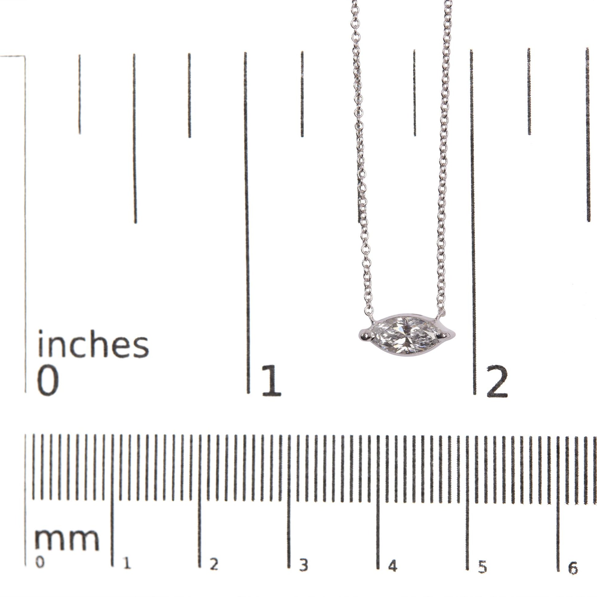 Close-up front view of white metal necklace with a marquise-shaped white gemstone in a 2-prong setting, placed on a ruler for size reference.