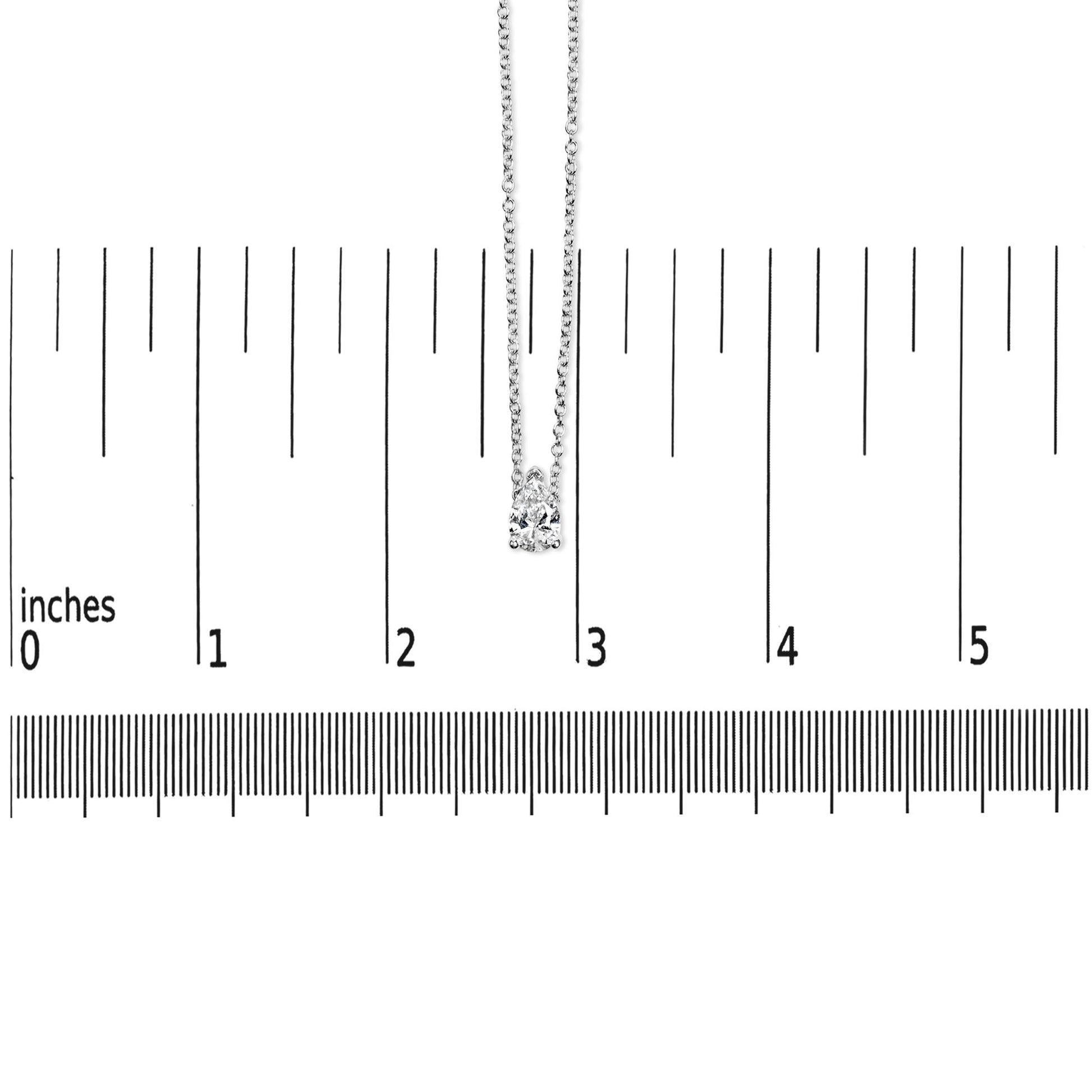White metal necklace with a pear-shaped white gemstone pendant in prong setting, shown hanging vertically on a ruler for size reference, front view.