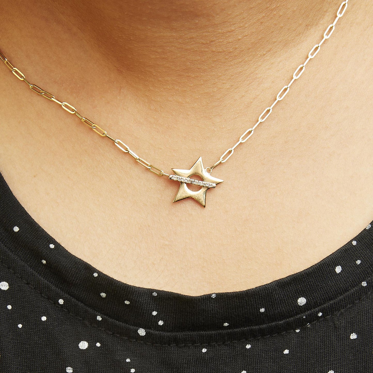 Yellow metal necklace with a star-shaped pendant featuring a horizontal row of white round gemstones in prong settings, shown worn on a model from a close-up front angle.