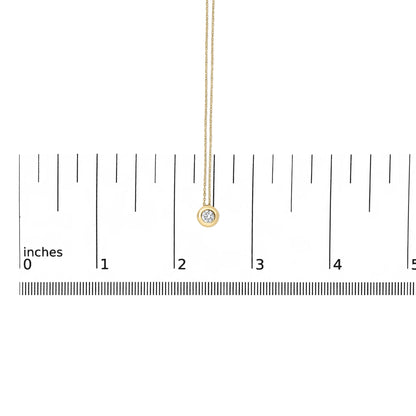 Close-up front view of a yellow necklace with a round white gemstone in a bezel setting, shown on a scale.
