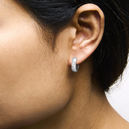 Close-up side view of a model wearing white metal hoop earrings featuring a pear-shaped white gemstone in bezel setting.
