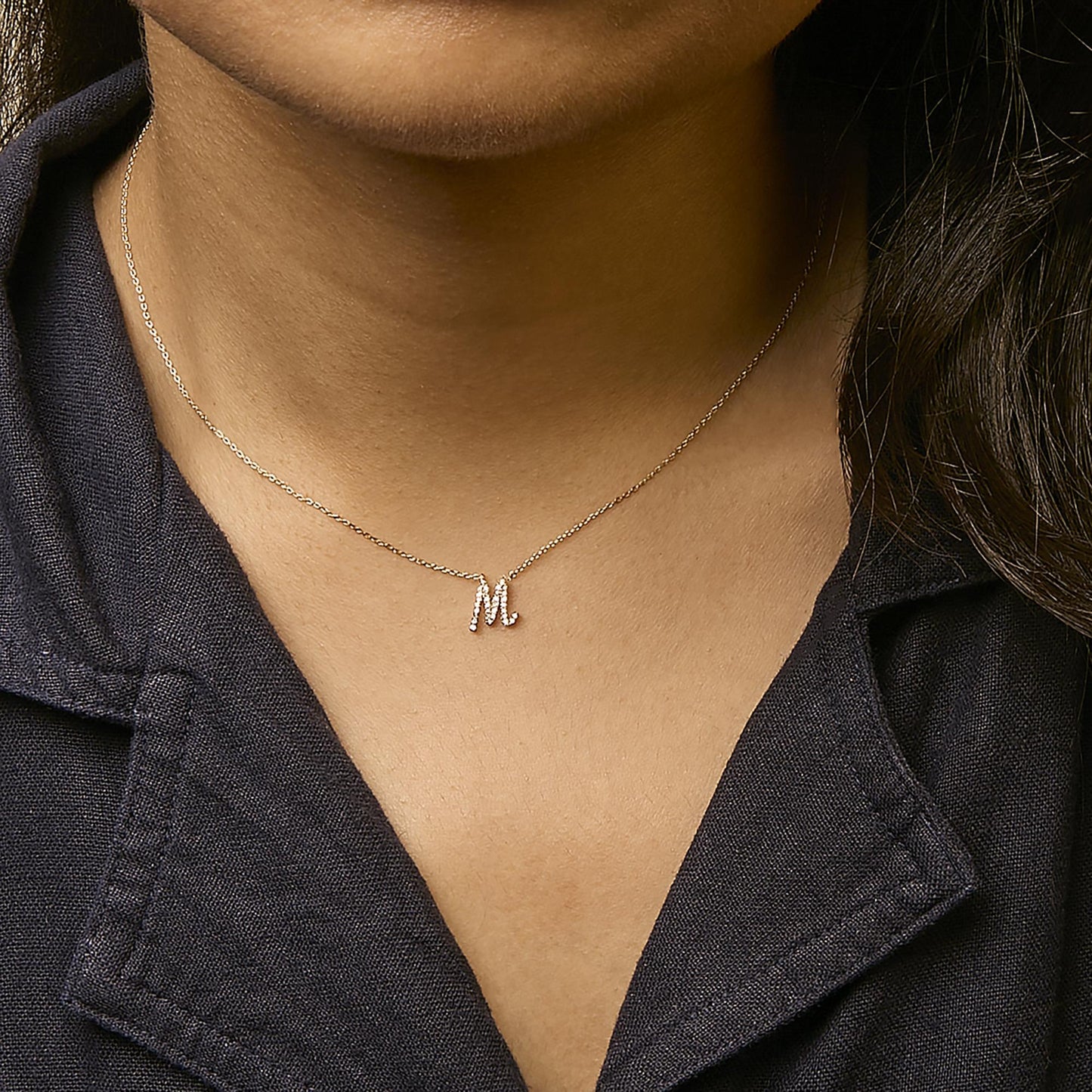 Close-up front view of a model wearing a delicate yellow necklace with a pendant in the shape of the letter 'M' adorned with small white gemstones in a micro-pave setting.