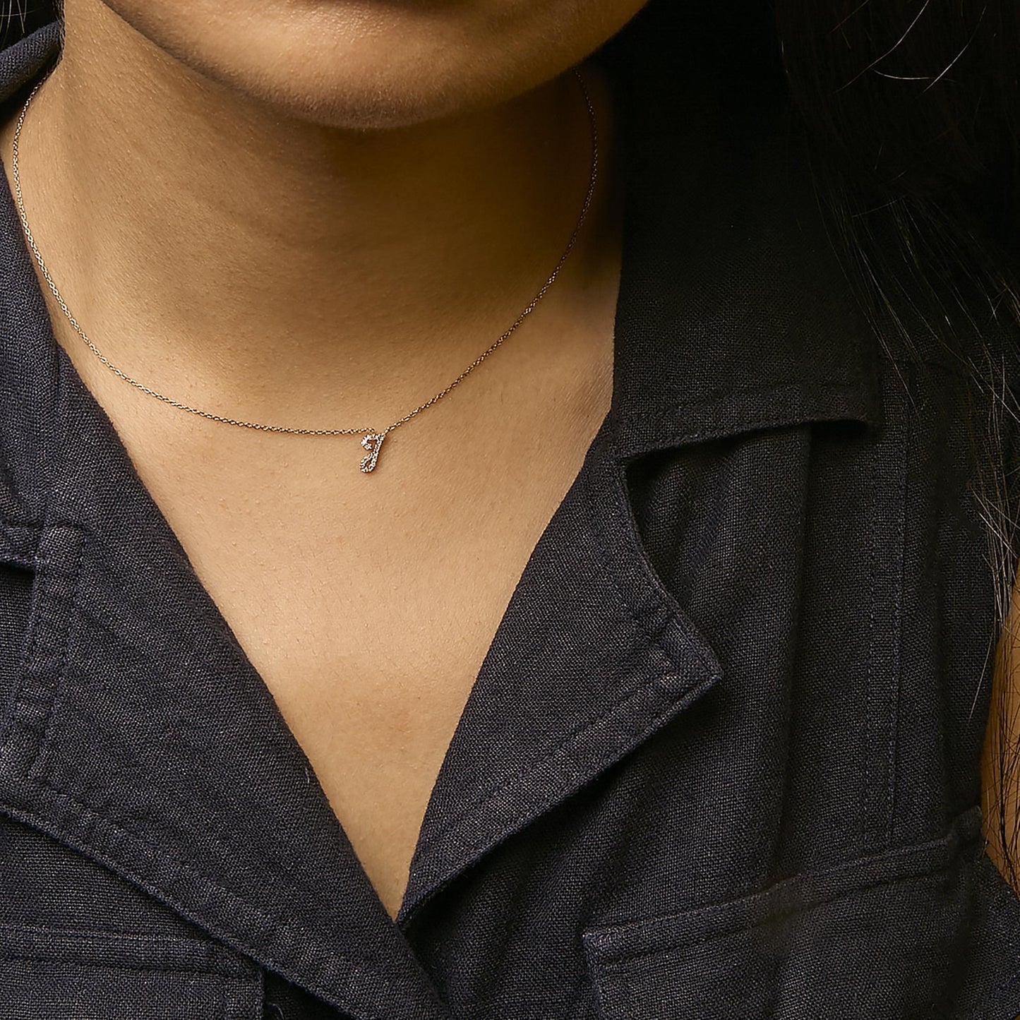 Close-up front view of a yellow metal necklace with a small pendant encrusted with round white gemstones in a micro-pave setting, worn on a model.