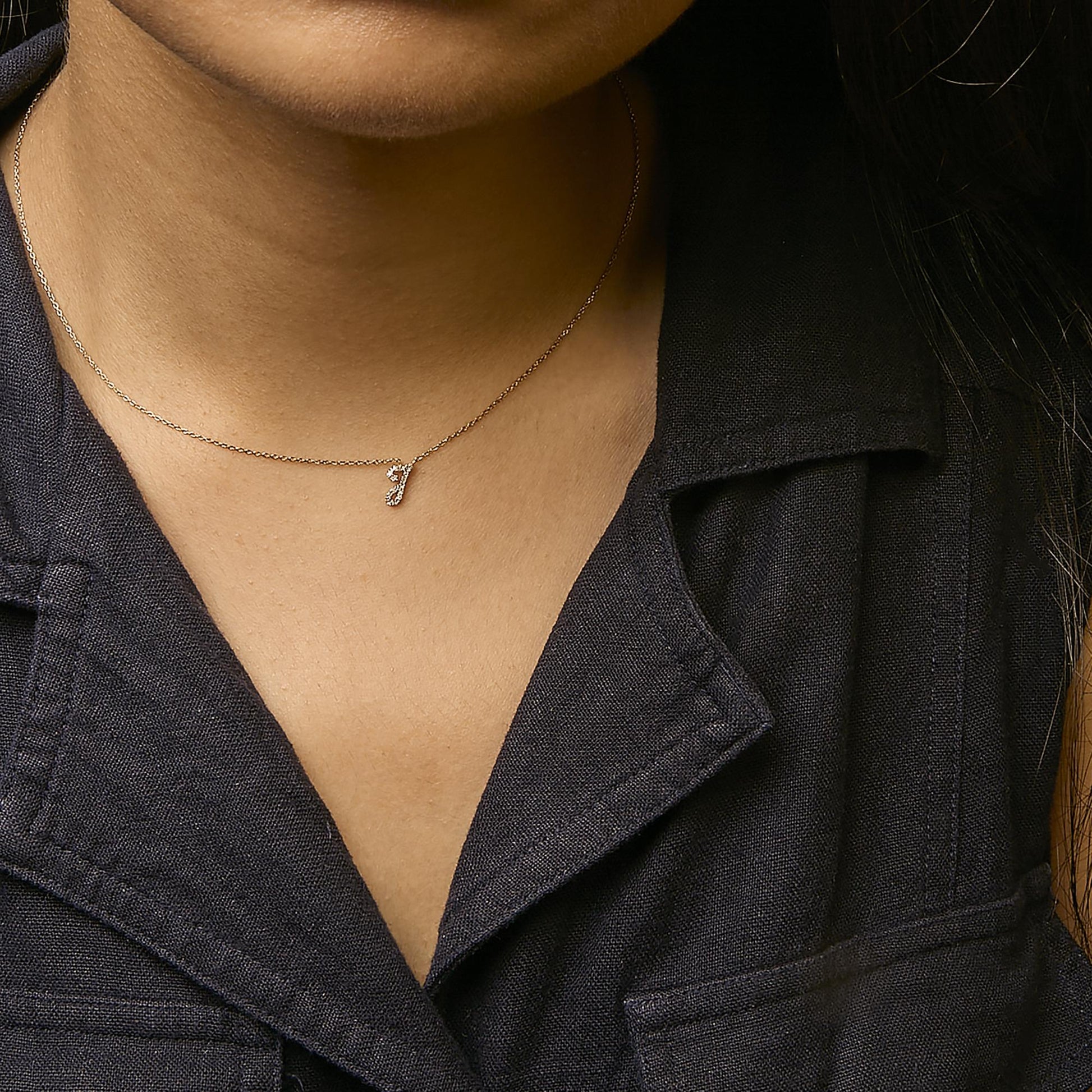 Close-up front view of a yellow metal necklace with a small pendant encrusted with round white gemstones in a micro-pave setting, worn on a model.