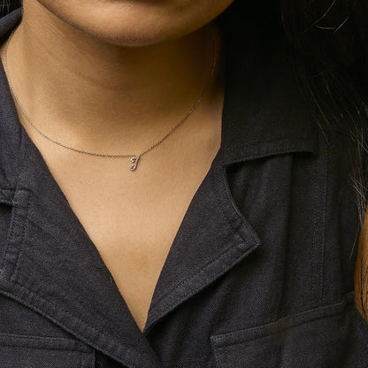 Close-up front view of a yellow metal necklace with a small pendant encrusted with round white gemstones in a micro-pave setting, worn on a model.