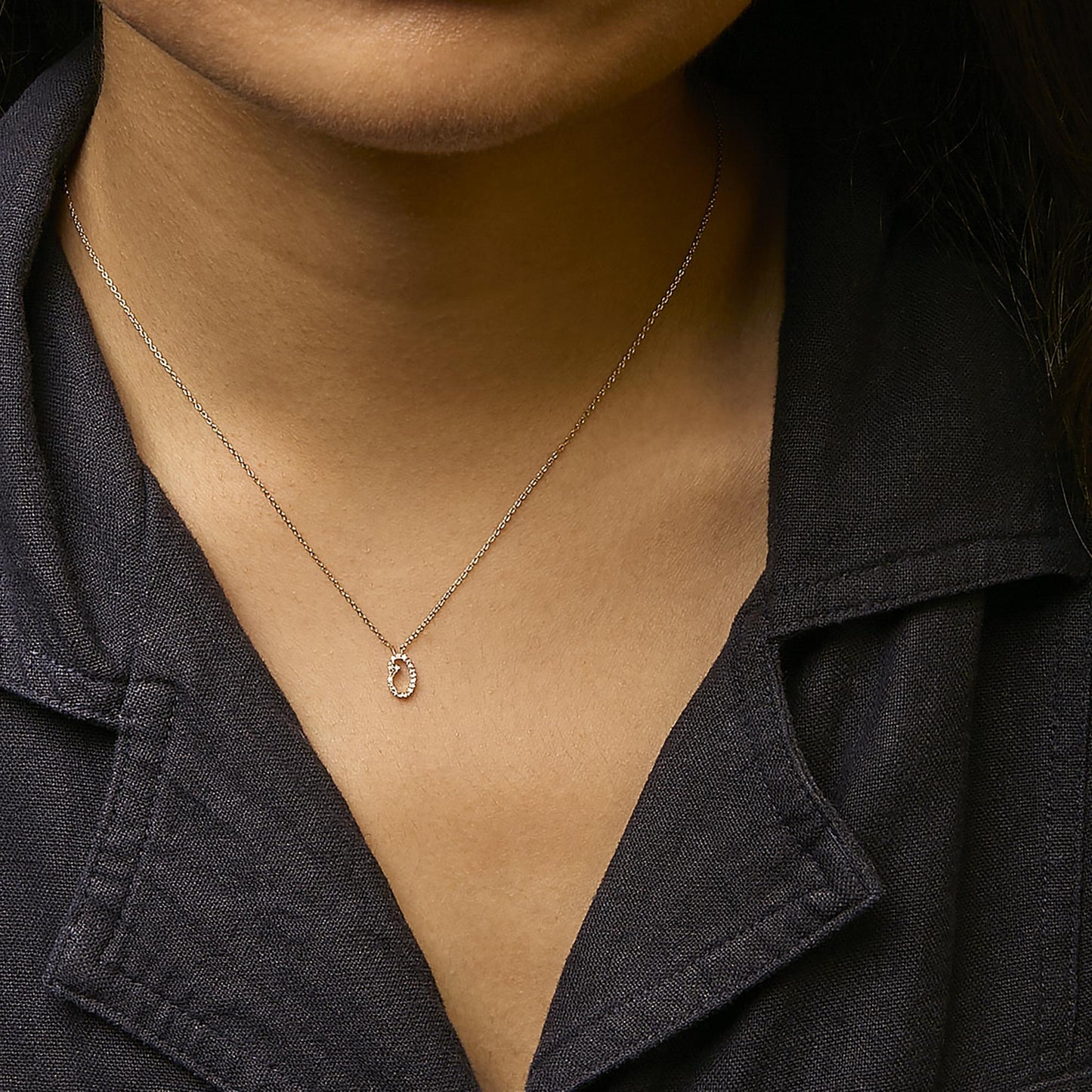 Close-up front view of a yellow metal necklace with an oval pendant featuring white round gemstones in a micro-pave setting, shown worn on a model.