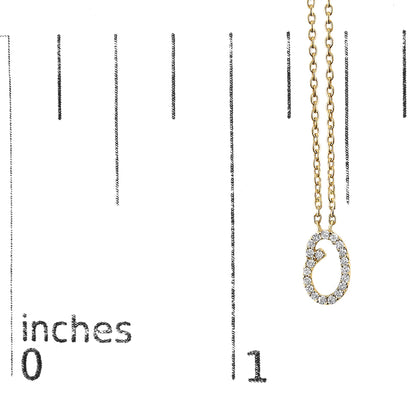 Yellow metal necklace with an oval-shaped pendant set with round white gemstones in a micro-pave setting, shown close-up on a scale with inch markings.