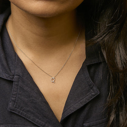 Close-up front view of a model wearing a yellow metal necklace with a pendant featuring a letter Q adorned with round white gemstones in micro-pave setting.