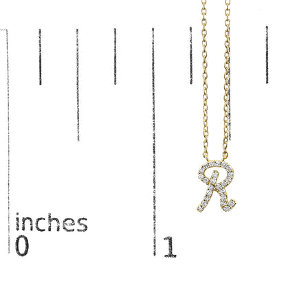 Close-up front view of a yellow necklace with a pendant shaped like the letter 'R' adorned with small white gemstones, shown on a measurement scale.