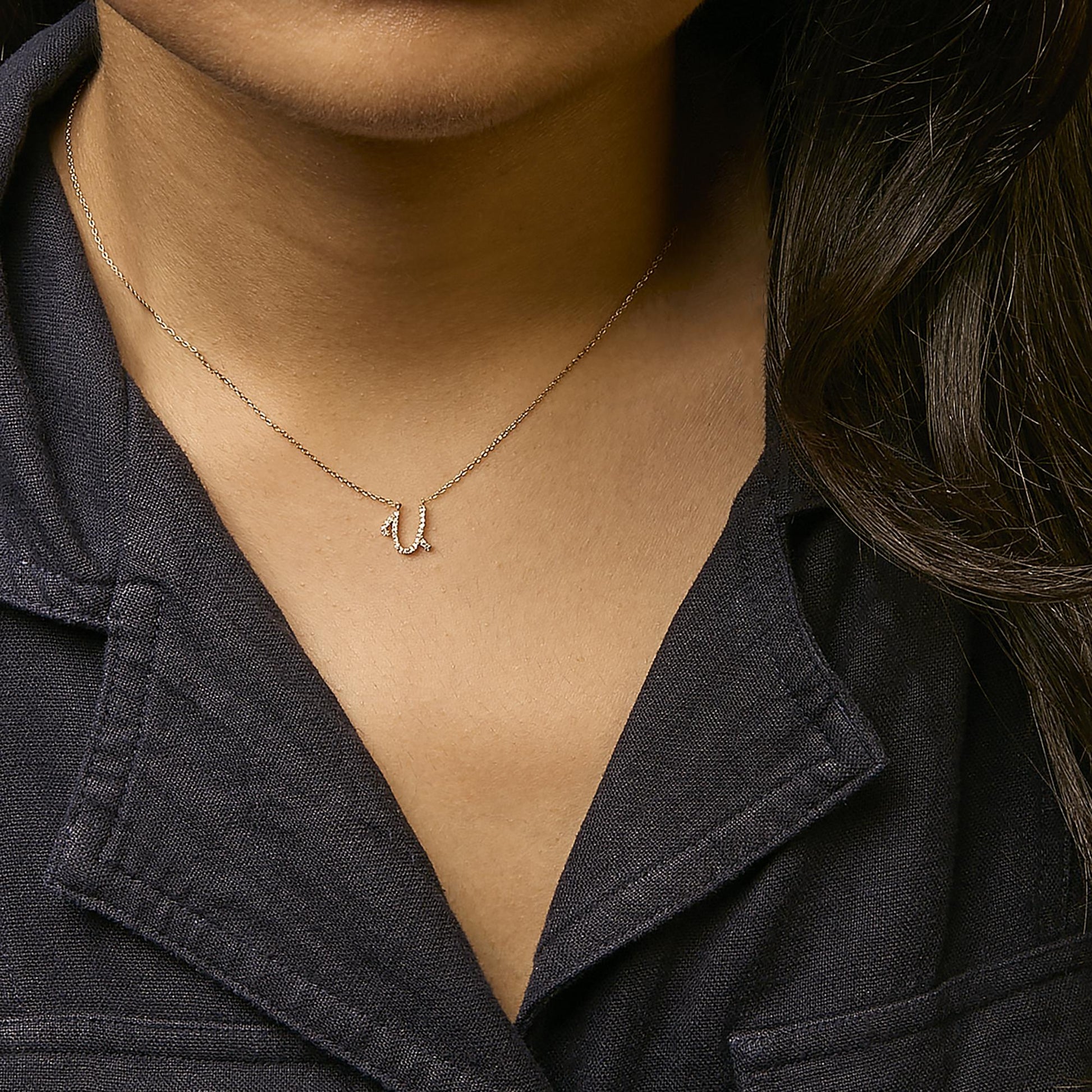 Close-up front view of a model wearing a delicate yellow metal necklace with a curved pendant featuring small round white gemstones in a micro-pave setting.