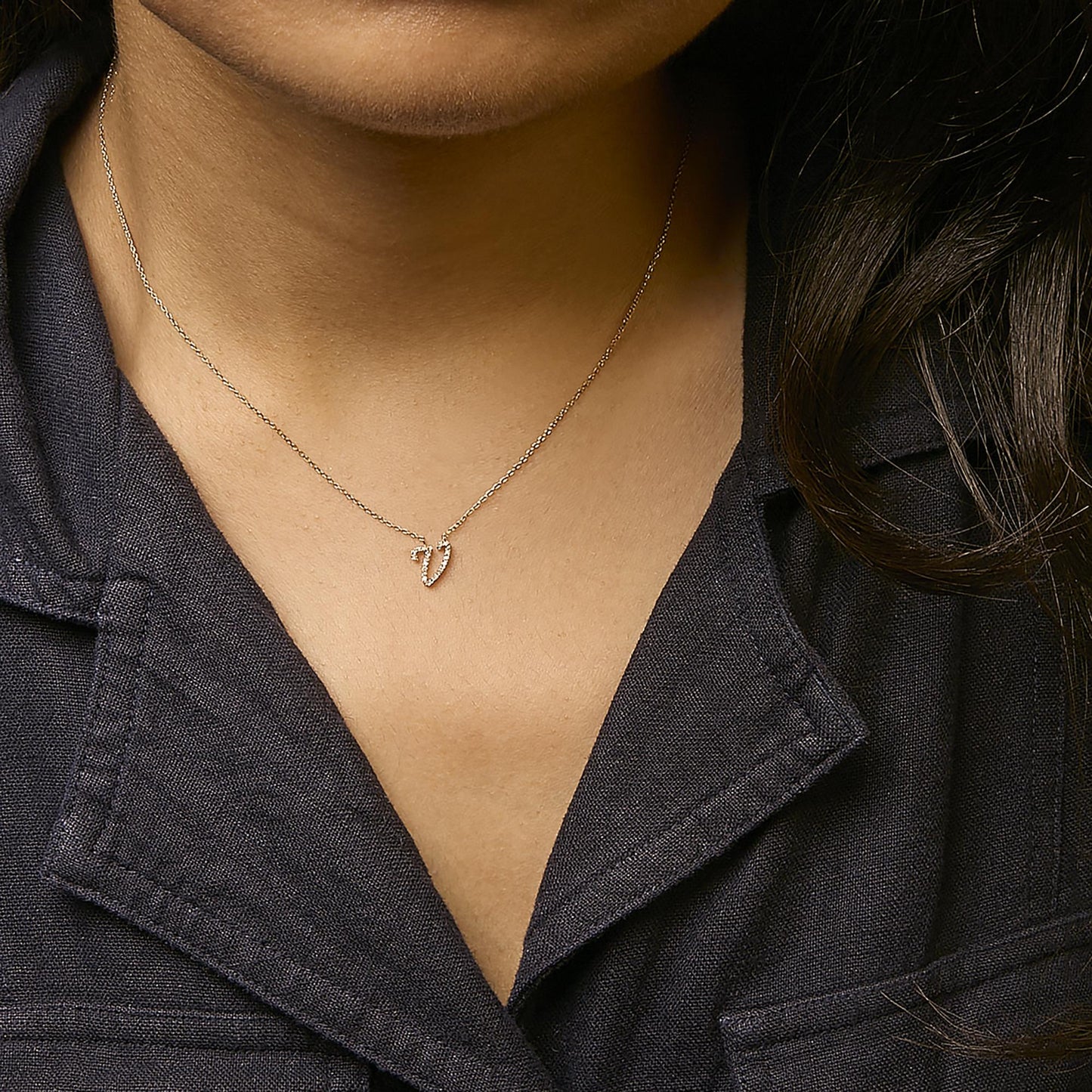 Yellow metal necklace with a small V-shaped pendant set with round white gemstones in micro-pave setting, shown worn on a model from a front close-up angle.