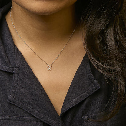 Yellow metal necklace with a pendant in micro-pave setting of round white gemstones, shown worn on a model from a front angle.