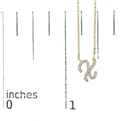 Close-up front view of a yellow metal necklace pendant in the shape of the letter X, adorned with white round gemstones in a micro-pave setting, shown on a scale.