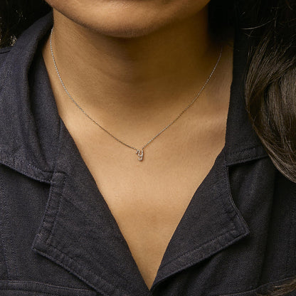 Close-up front view of a necklace with a yellow chain and a small pendant featuring round white gemstones in a micro-pave setting, worn by a model.