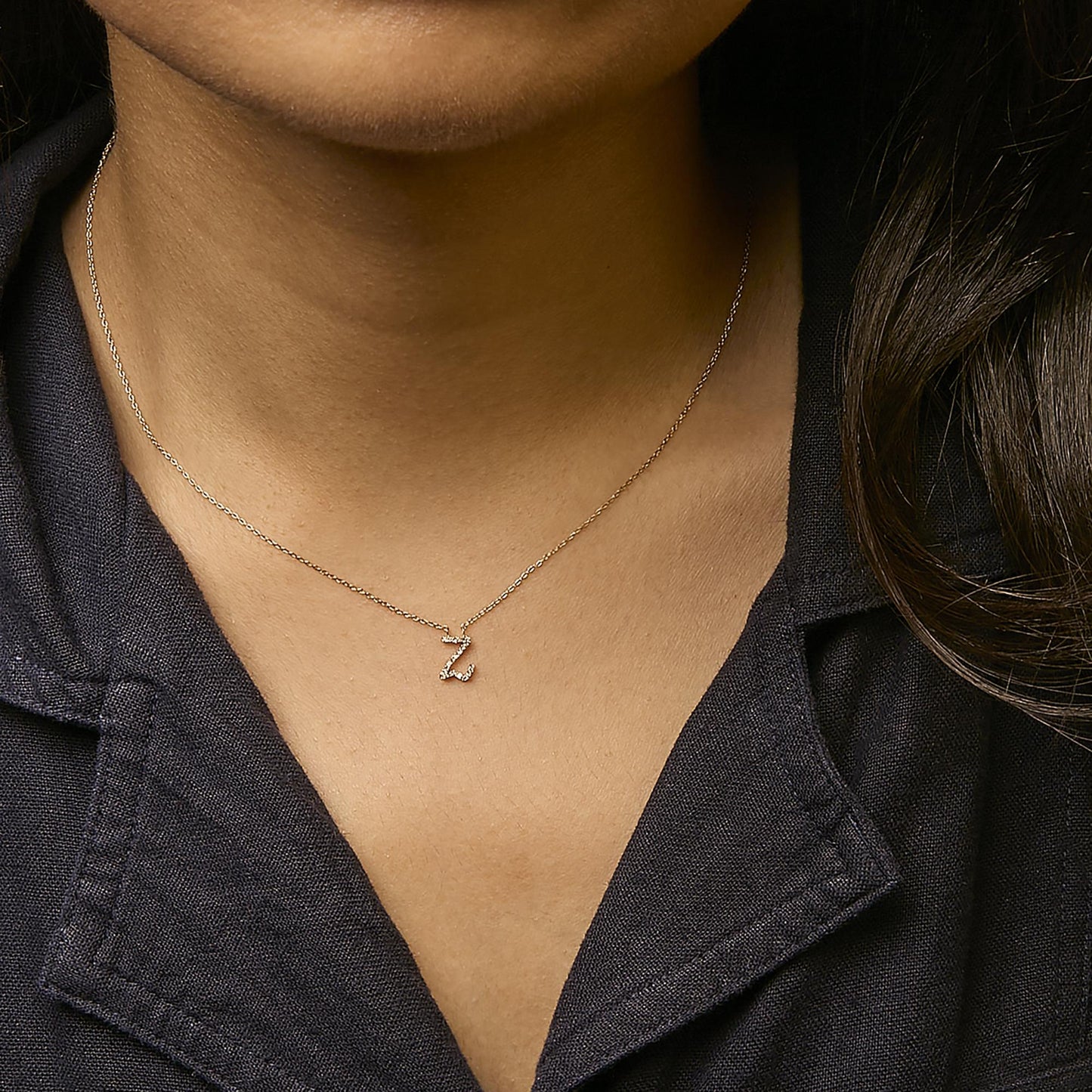 Close-up front view of a yellow necklace with a pendant in a zigzag shape set with small white round gemstones, shown worn on a model.