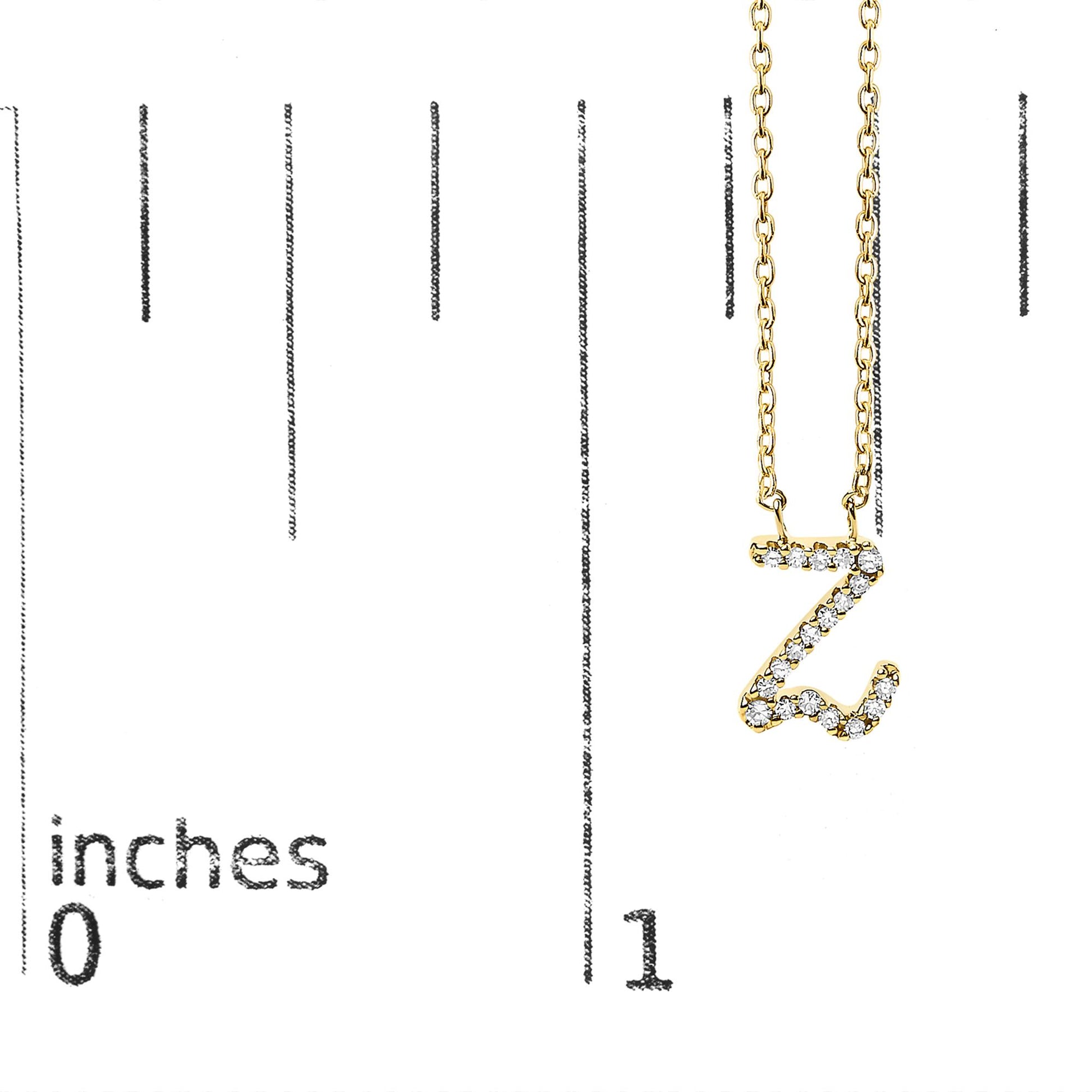 Close-up front view of a yellow metal necklace with a pendant shaped like the letter Z, adorned with small white gemstones in a micro-pave setting, shown on a scale with inch markings.