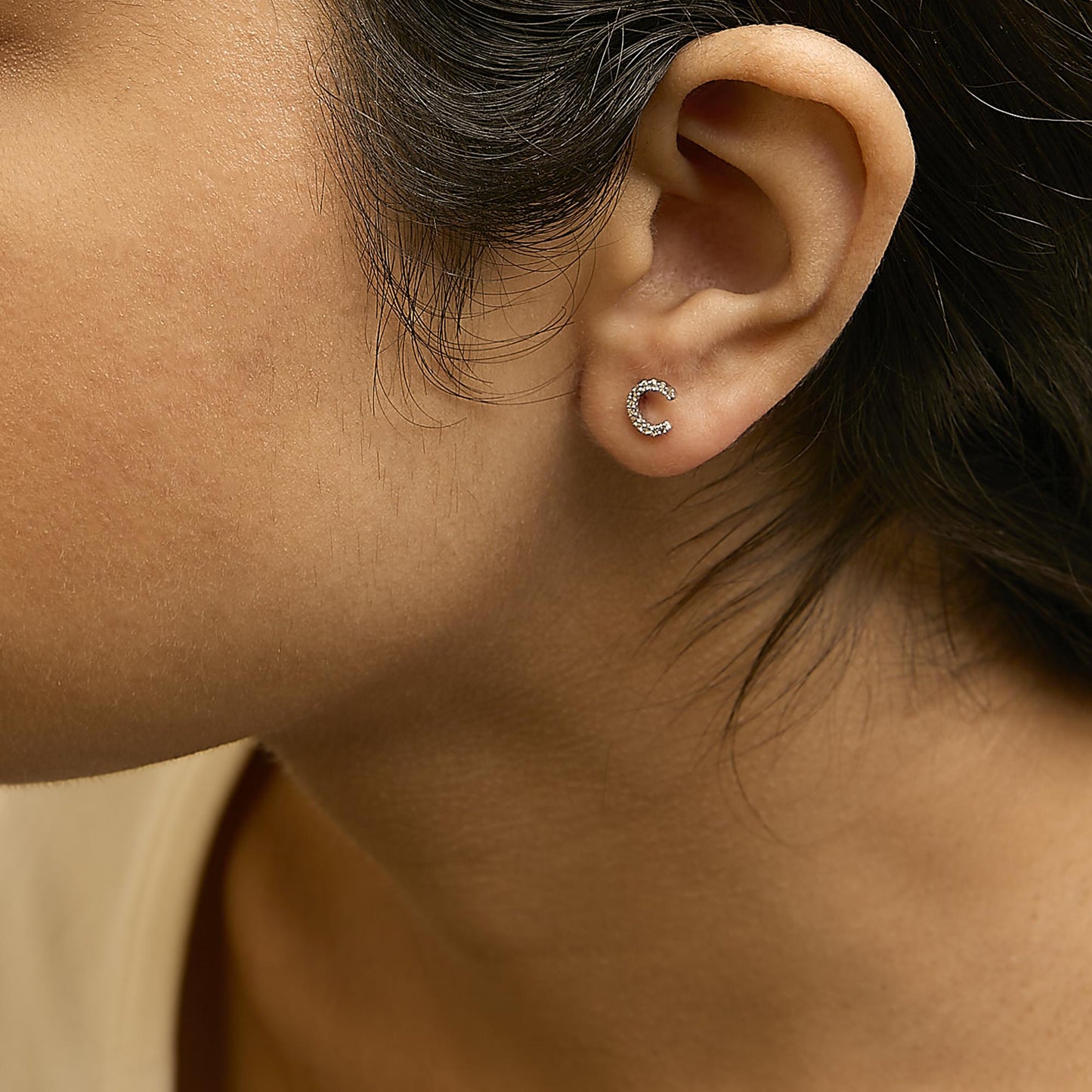 Close-up side view of a model wearing small white metal crescent-shaped earrings with white round gemstones in a micro-pave setting.