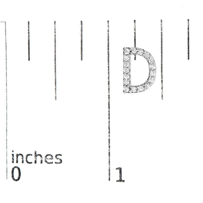Close-up of a single white metal earring shaped like the letter D, set with small white gemstones in a micro-pave style, shown on a scale with inch markings.