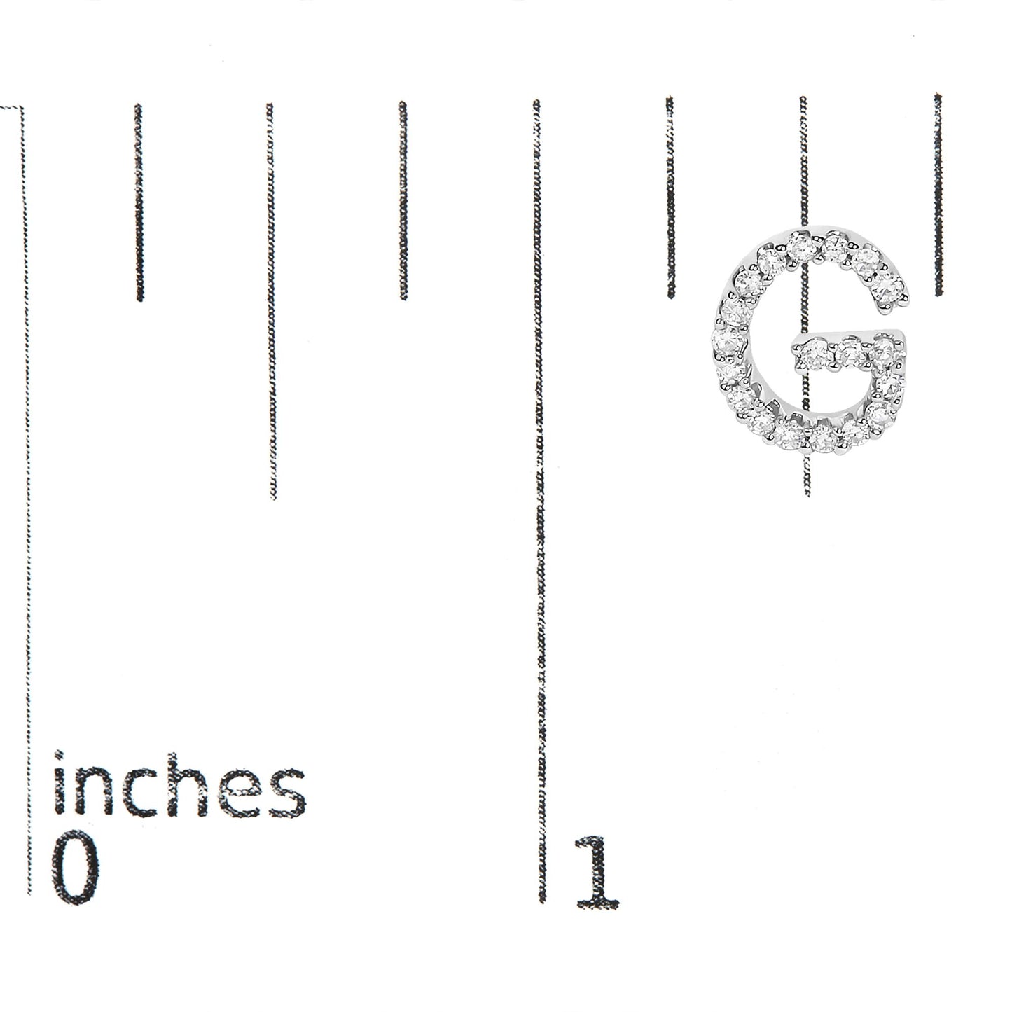 Close-up top-down view of a white metal earring shaped like the letter G, covered in small white gemstones, shown on a scale marked in inches.