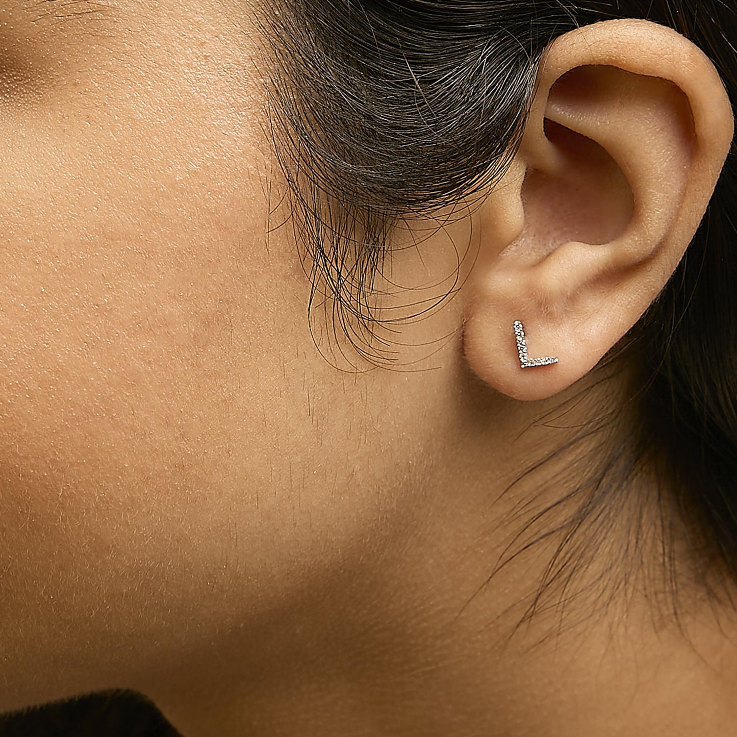 Close-up side view of a model wearing a white metal L-shaped stud earring with small round white gemstones in a micro-pave setting.