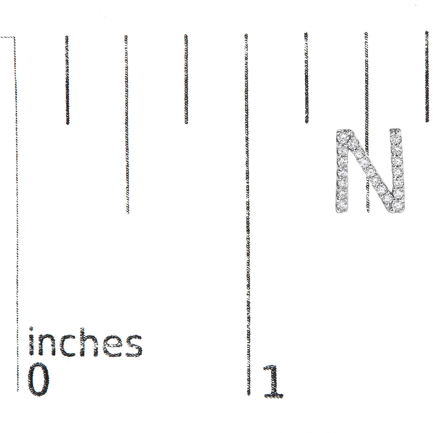 White metal earring shaped like the letter N, covered with small white gemstones, shown on a scale from a front angle.