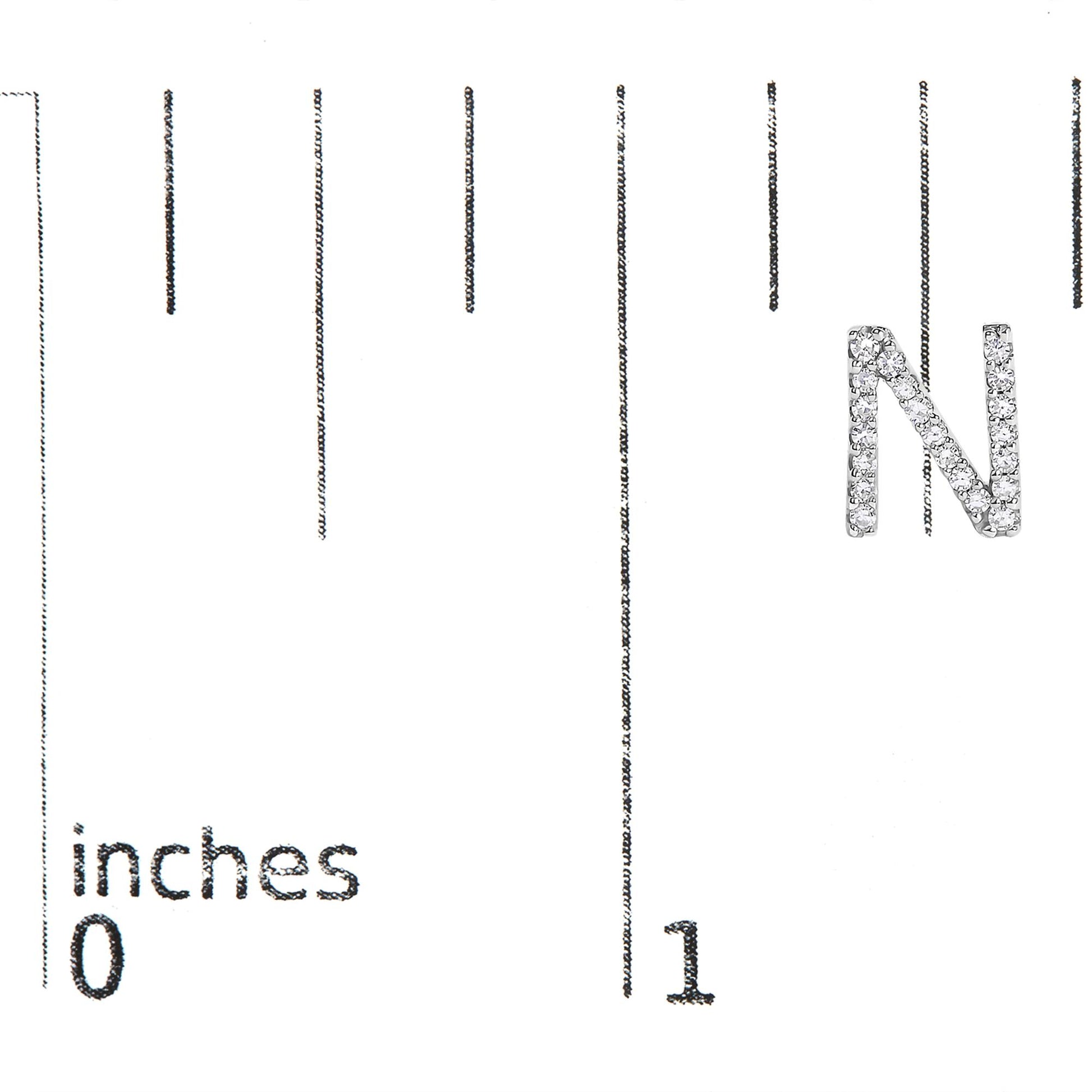 White metal earring shaped like the letter N, covered with small white gemstones, shown on a scale from a front angle.