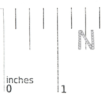 White metal earring shaped like the letter N, covered with small white gemstones, shown on a scale from a front angle.