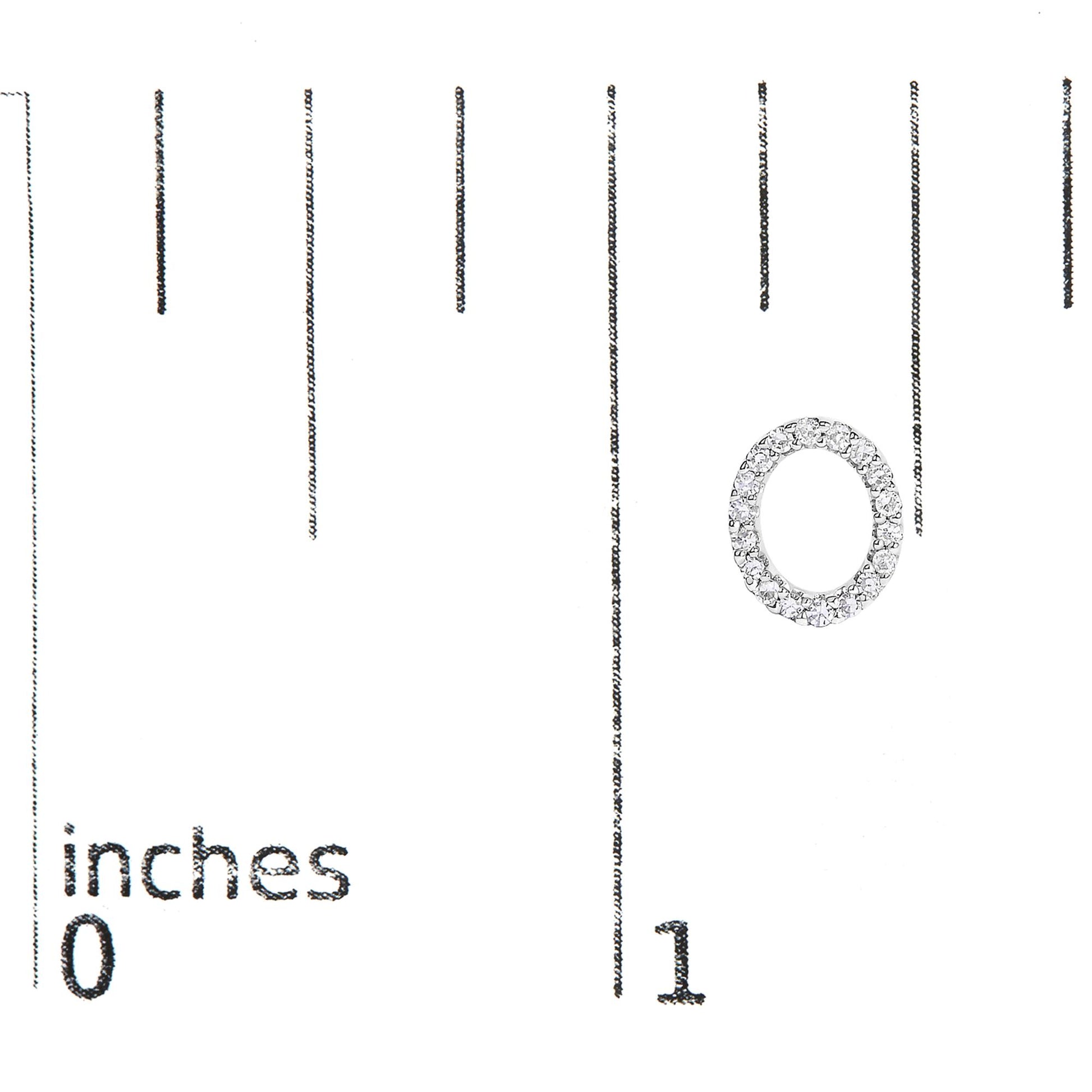 Close-up of a white circular earring with white round gemstones in a micro-pave setting, shown on a scale with inch markings.