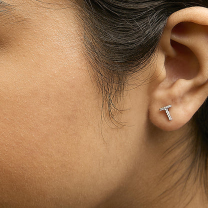 Close-up side view of a model wearing a white metal earring in the shape of a 'T' adorned with small round white gemstones in a micro-pave setting.