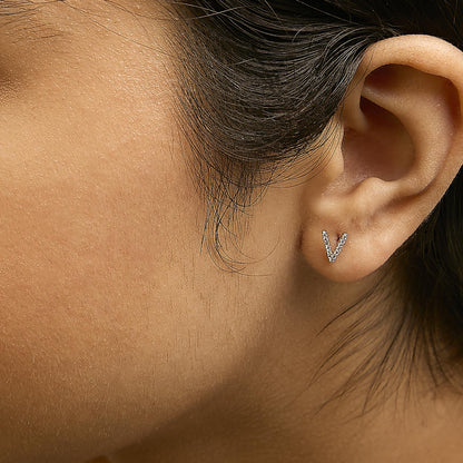 Close-up side view of a model wearing a white metal V-shaped earring encrusted with small round white gemstones in a micro-pave setting.